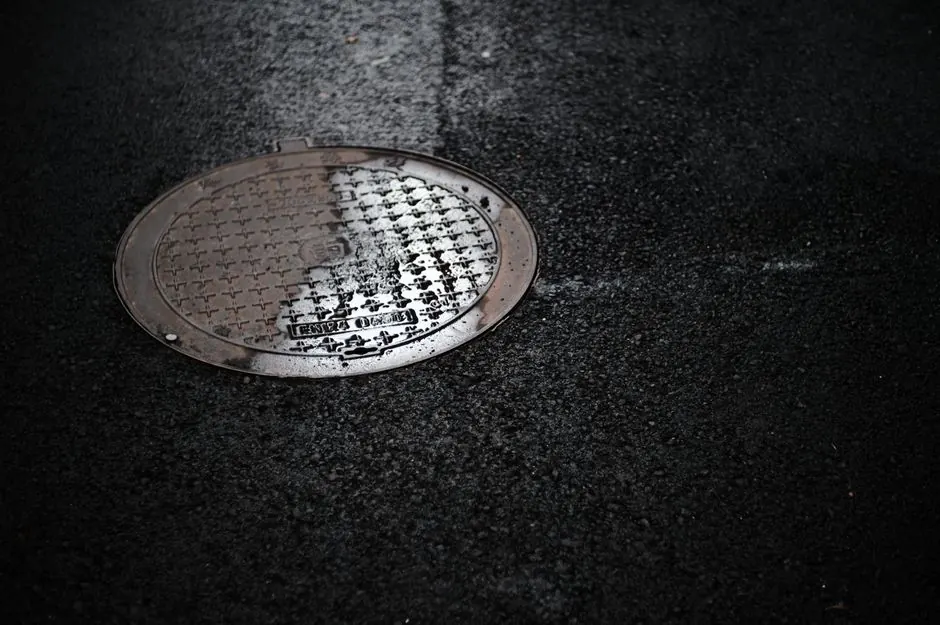 Close-up of a wet manhole cover on a rainy urban street, reflecting light.